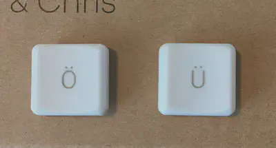 a picture of 2 keycaps with &lsquo;Ö&rsquo; and &lsquo;Ü&rsquo; on them, looking like a surprised and smiling face respectively