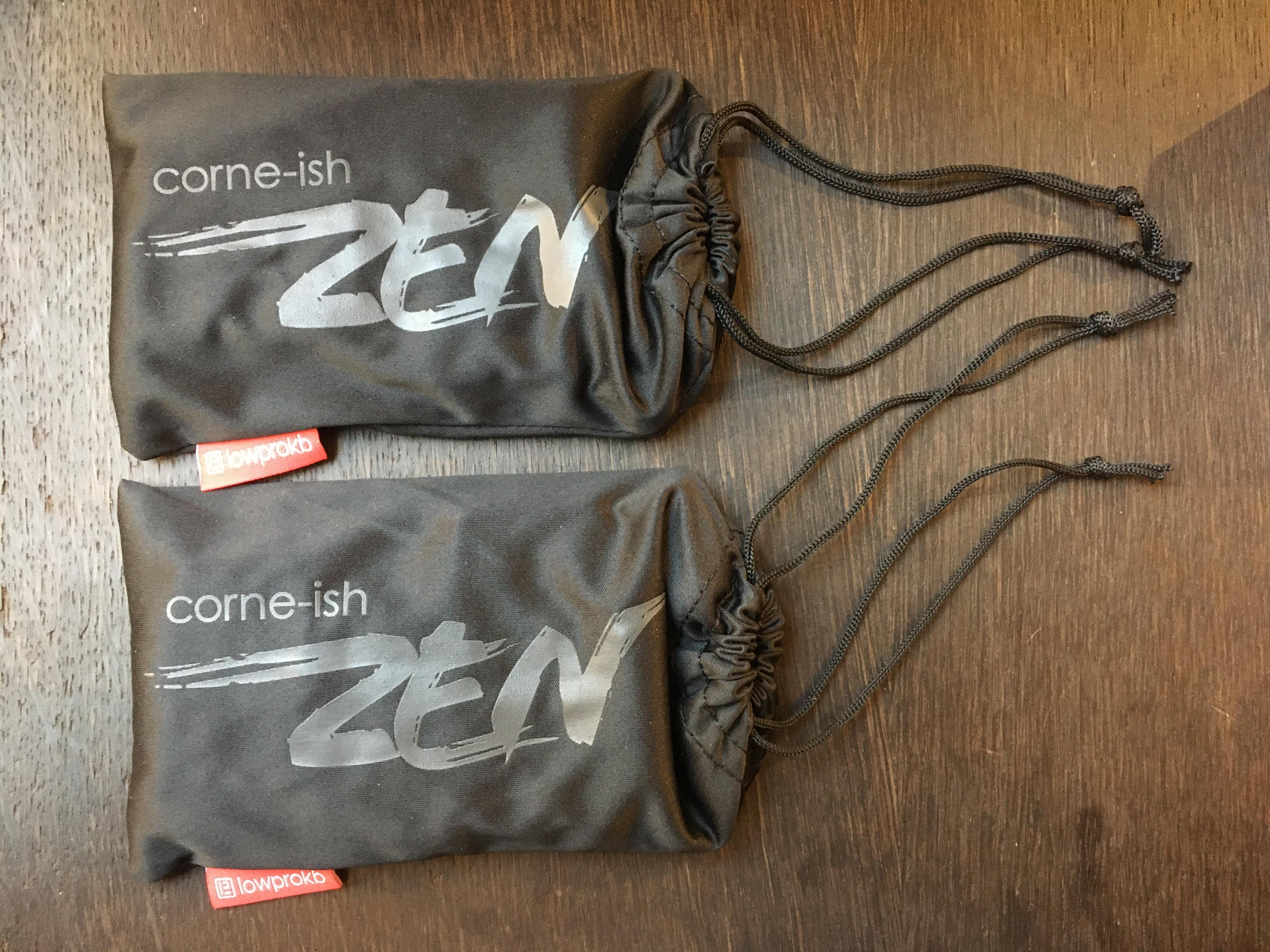 An image of two fabric pouches on a table. The pouches have a stylized &ldquo;Corne-Ish Zen&rdquo; printed on them.